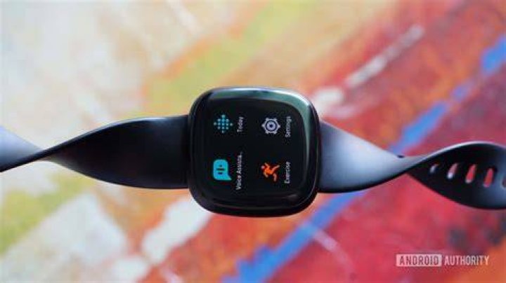 A Fitbit Versa 3 rests on a blue surface displaying the Shut Down confirmation screen.