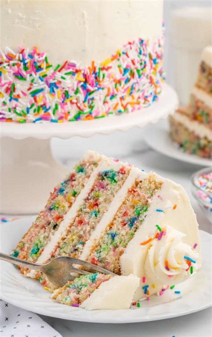 A slice of funfetti cake surrounded by rainbow confetti and rose wine