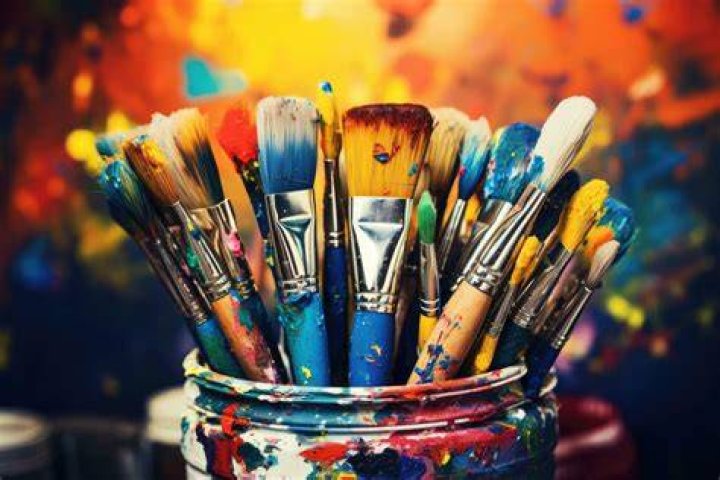 A table covered with paintbrushes, paint, and a water cup