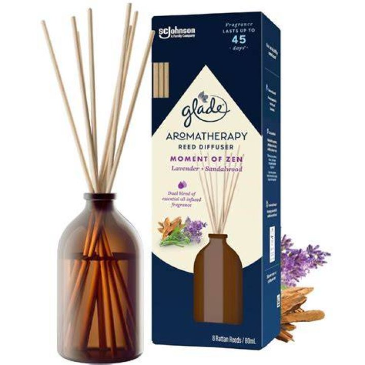 An aromatherapy reed diffuser in front of a rolled-up towel and two candles