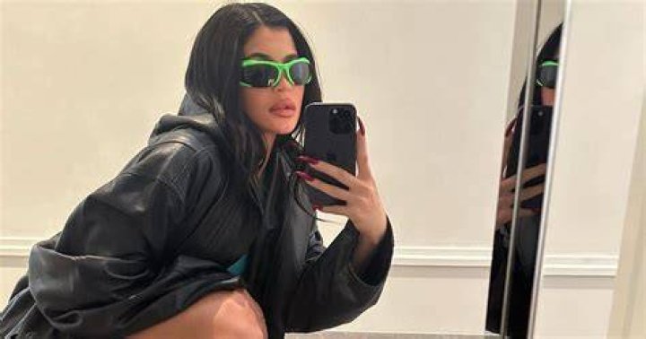Kylie Jenner taking a mirror selfie as Travis Scott hugs her from the side.